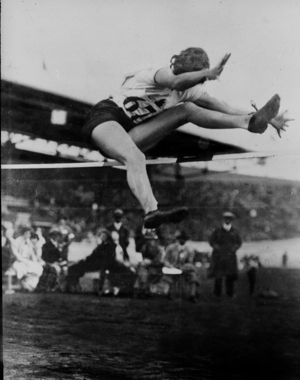 Photo en noir et blanc d'une femme qui saut par dessus une barre. 