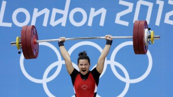 Christine Girard soulève une barre d'haltérophilie devant les anneaux olympiques.