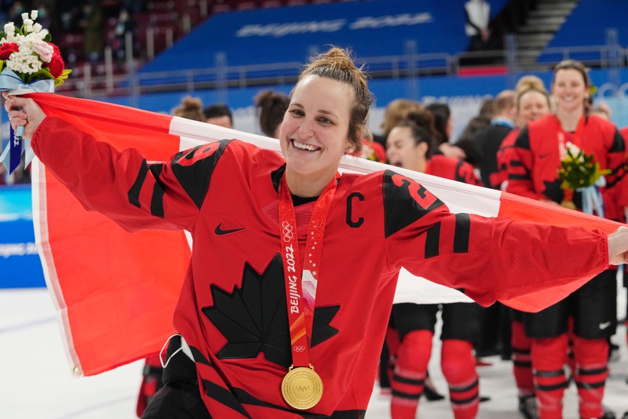 Marie-Philip Poulin élance le drapeau canadien dans les airs derrière elle, tandis qu'elle porte sa médaille d'or au cou gagnée lors de la finale contre les États-Unis à Beijing 2022