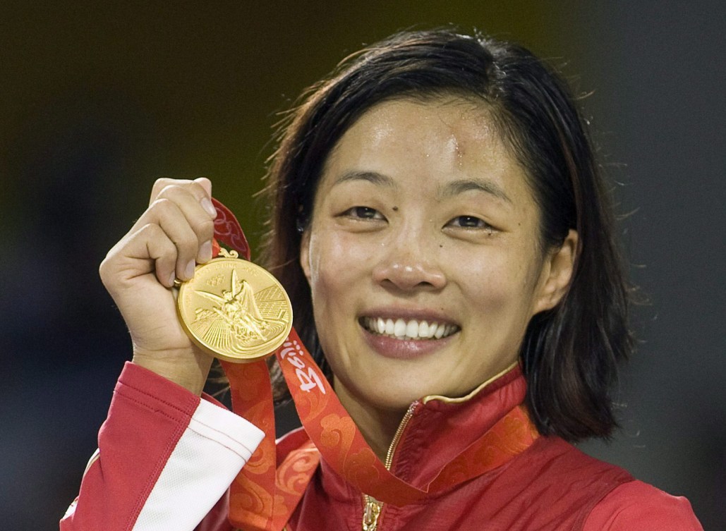 Une athlète tient une médaille d'or à côté de son visage. 
