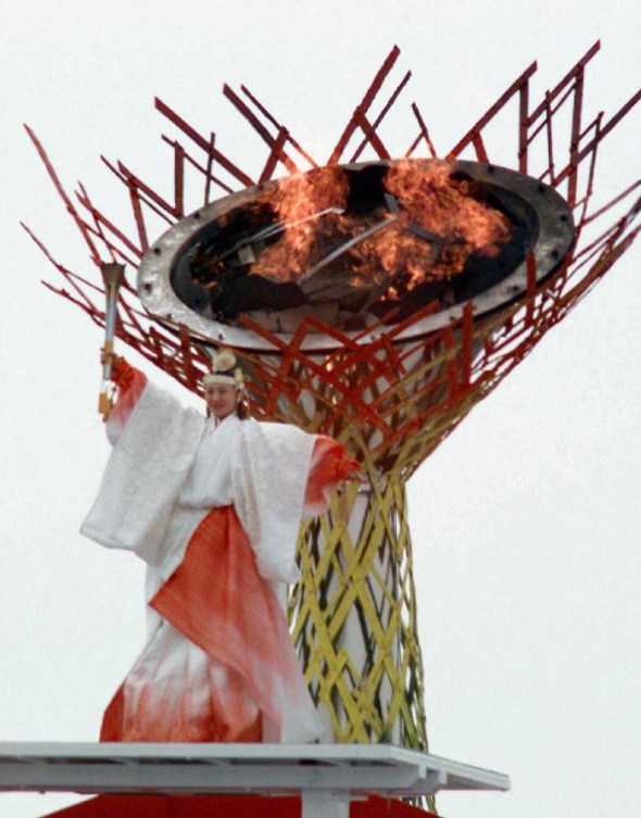 Une femme dans des habits traditionnels japonais devant la vasque olympique.