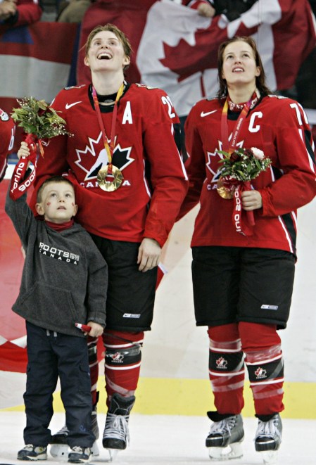 Hayley Wickenheiser du Canada, à gauche, son fils Noah et Cassie Campbell, lèvent les yeux tandis qu'ils élèvent le drapeau canadien pendant la cérémonie des médailles aux Jeux olympiques d'hiver de 2006, le 20 février 2006 , À Turin, en Italie. (AP Photo / Gene J. Puskar)