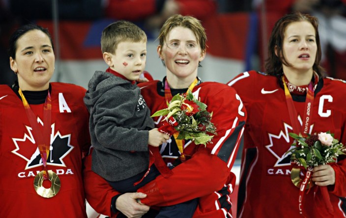 Hayley Wickenheiser d'Équipe Canada tient son fils, Noah, et chante l'hymne avec Vickey Sunohara, à gauche, et Cassie Campbell, à droite, fête après avoir vaincu la Suède 4-1 pour remporter la médaille d'or aux Jeux olympiques de 2006, le 20 février 2006 à Turin. (CP PHOTO / Ryan Remiorz)