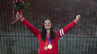 Christine Girard avec une médaille d'or olympique et une médaille de bronze olympique autour du cou lève les bras dans les airs.