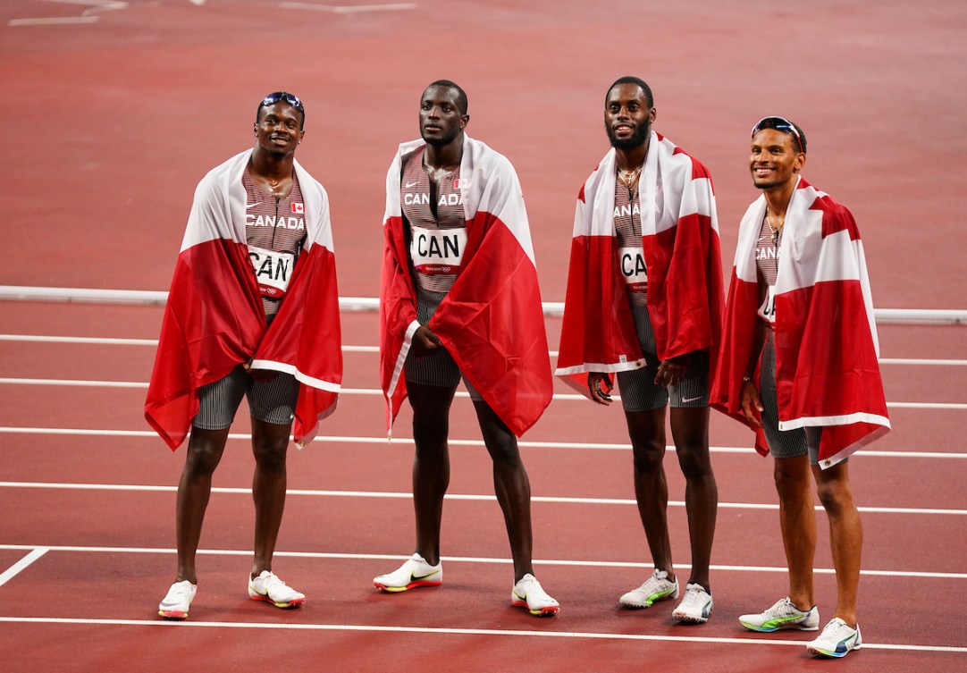 Aaron Brown, Jerome Blake, Brendon Rodney et Andre De Grasse sur la piste d'athlétisme avec des drapeaux canadiens sur les épaules.