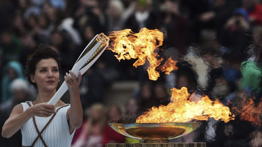 Une femme vêtue en citoyenne de la Grèce antique allume la flamme olympique