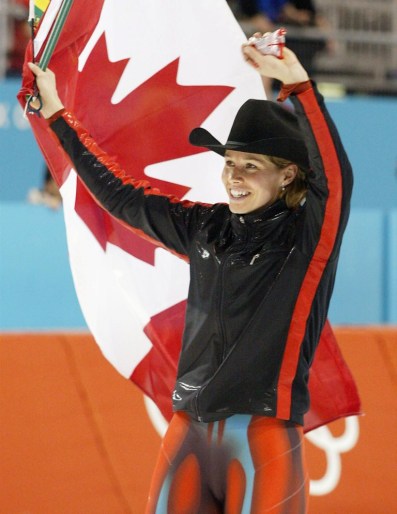 Une patineuse de vitesse célèbre sa victoire en bradissant le drapeau canadien et en portant un chapeau de cowboy