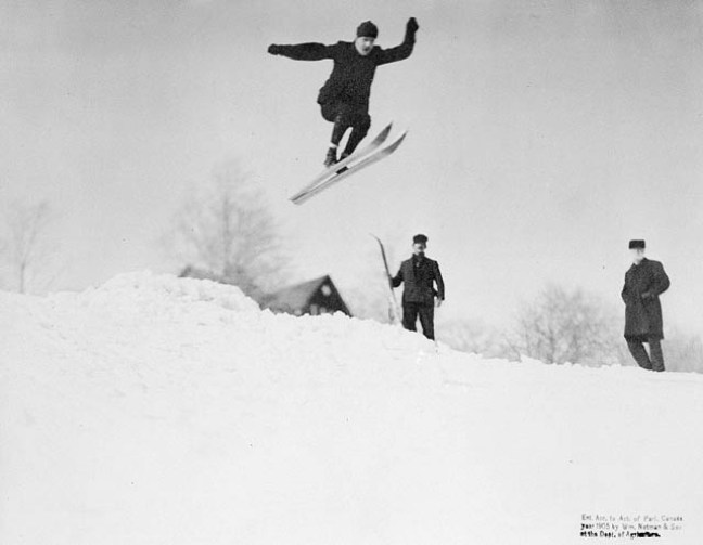 un skieur des années 1900 effectue un saut depuis une butte de neige
