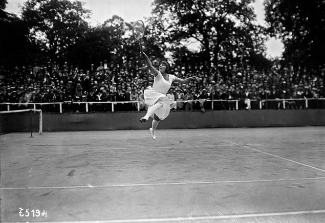 Une joueuse de tennis des années 1920 dans une grande robe blanche saute pour atteindre la balle