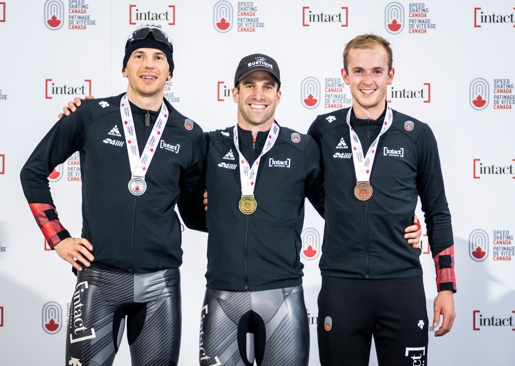 Les trois patineurs médaillés posent sur le podium avec leur médaille au cou.