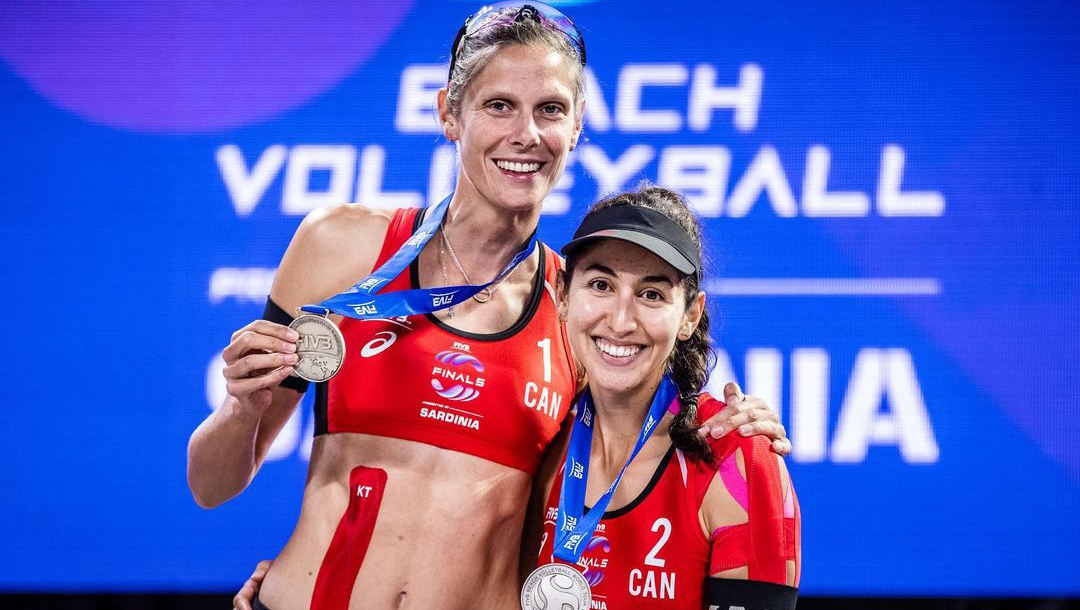 Deux joueuse de volleyball de plage avec des chandails à manches longues s'enlacent avec leur médaille d'argent au cou en souriant et en regardant vers la caméra.