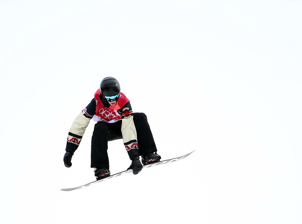 Un athlète de snowboard dans les airs touche sa planche d'une main. 