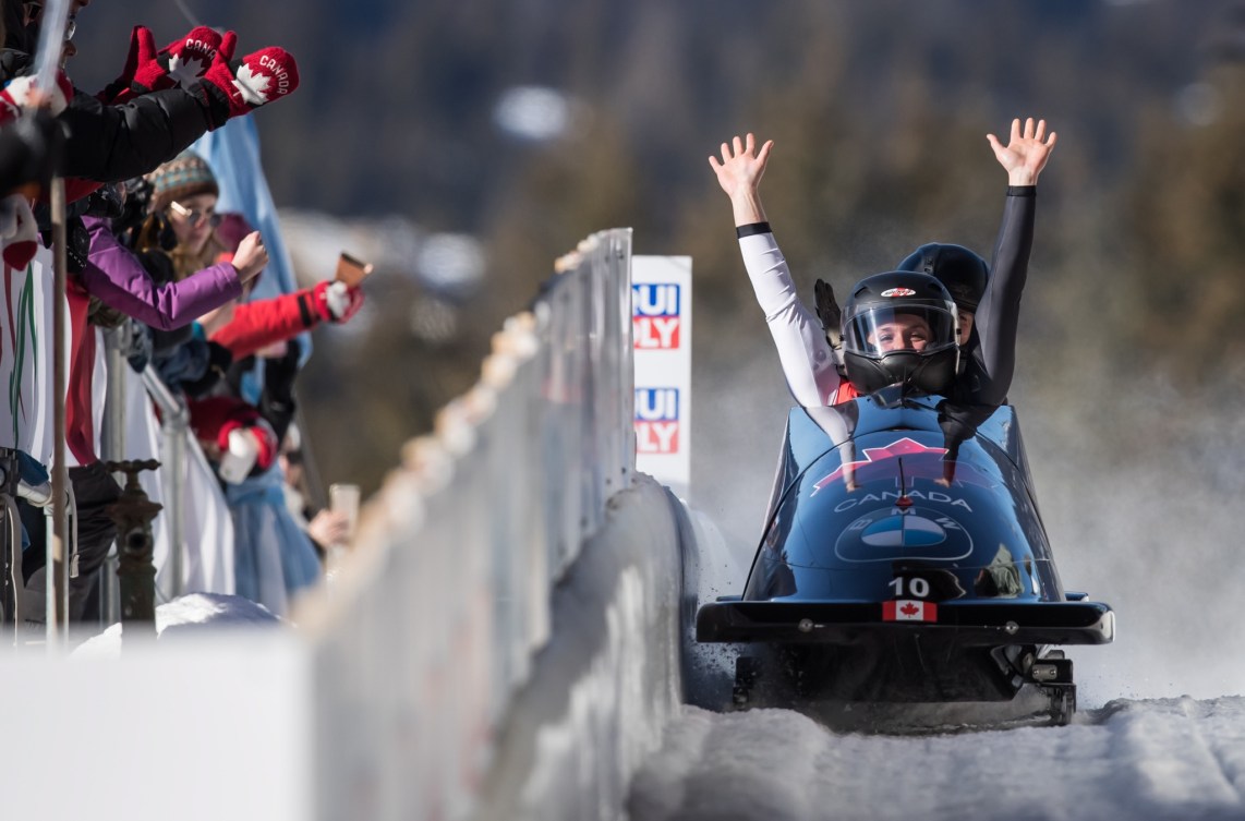 Deux athlètes de bobsleigh sont assises dans le bobsleigh à la fin d'une course. Une athlète a les deux bras dans les airs. 