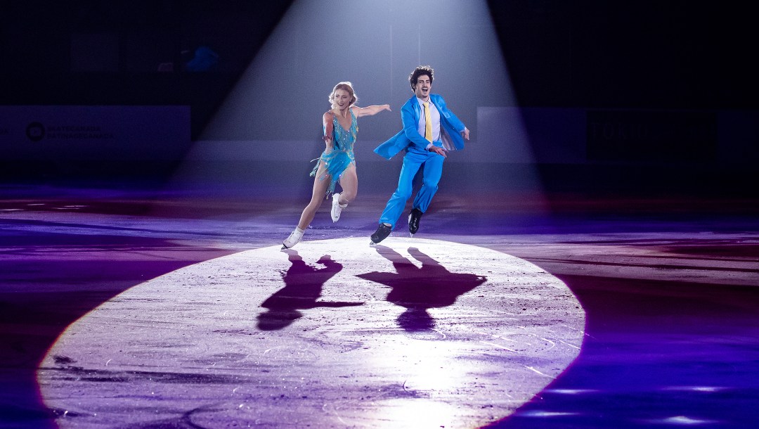 Deux patineurs sous la lumière d'un projecteur avec des costumes dans une teinte de bleu.