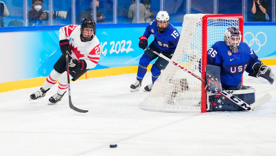 Deux joueuses de hockey en action derrière le filet avec la gardienne de but qui surveille la rondelle