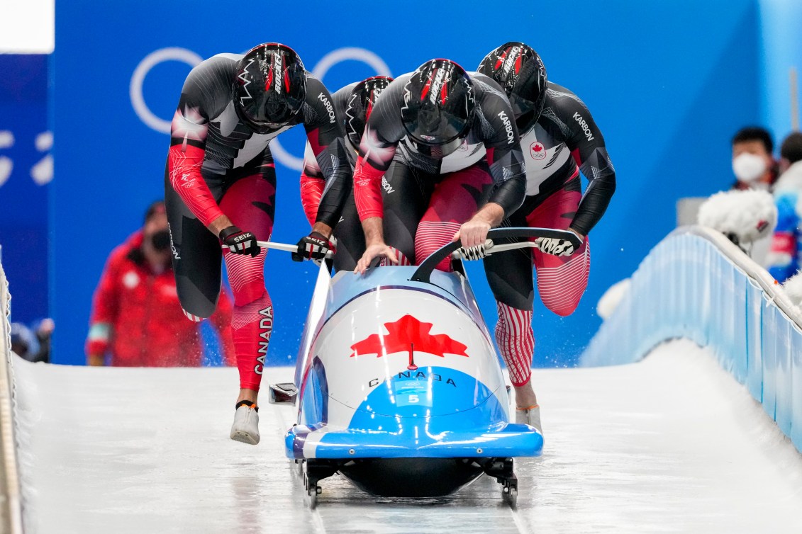 Justin Kripps, Ryan Sommer, Cam Stones et Benjamin Coakwell de Équipe Canada poussent sur la glace leur bob et deux d'entre eux sont déjà entrés en train de prendre position à l'intérieur. Le bob est bleu et blanc avec une feuille d'érable rouge sur le devant.