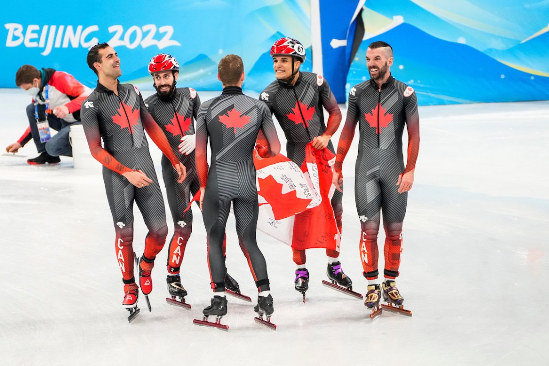 L'équipe masculine du relais masculin en patinage de vitesse sur courte piste célèbre sa victoire avec le drapeau canadien