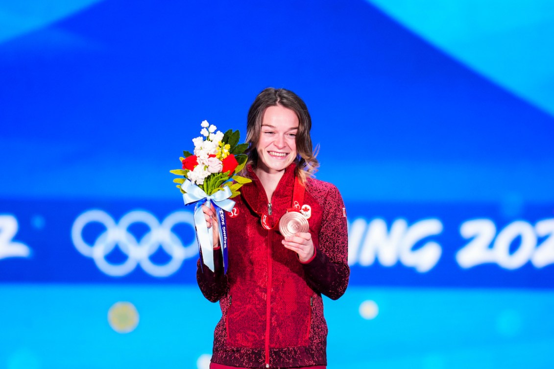 La patineuse de vitesse canadienne Kim Boutin sur le podium du 500 m courte piste. Elle soulève sa médaille de bronze avec la main gauche et tient son bouqut de fleurs avec la main droite. 