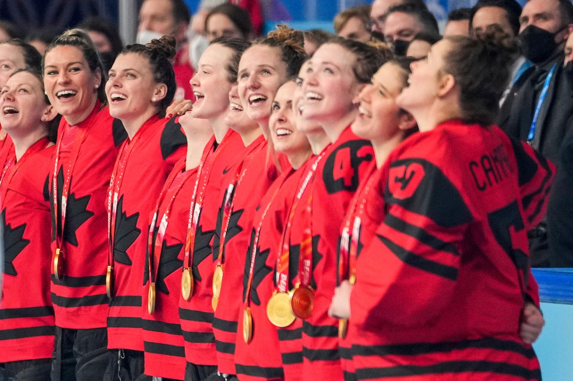 Les joueuses d'Équipe Canada sont bras dessus bras dessous, la médaille d'or autour du cou et chantent l'hymne national canadien, après leur victoire en finale en hockey féminin à Beijing 2022.