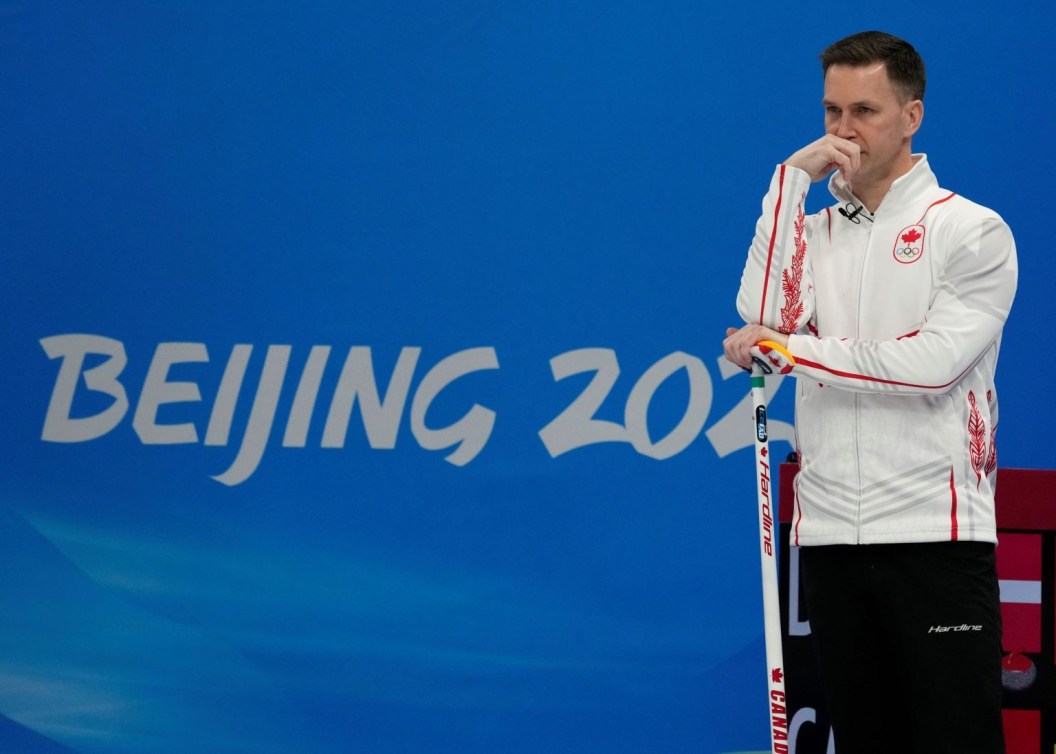Brad Gushue regarde devant lui, une main sur son balais, le coude appuyé sur le manche et le poign à la bouche, l'air penseur, lors du match de curling contre le Danemark