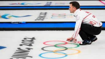 Accroupi, les mains appuyées sur le sol, Brad Gushue observe vers l'avant avec fébrilité sa pierre lancée et balayée par ses coéquipiers lors du match de curling contre la Suède en demi-finale à Beijing 2022