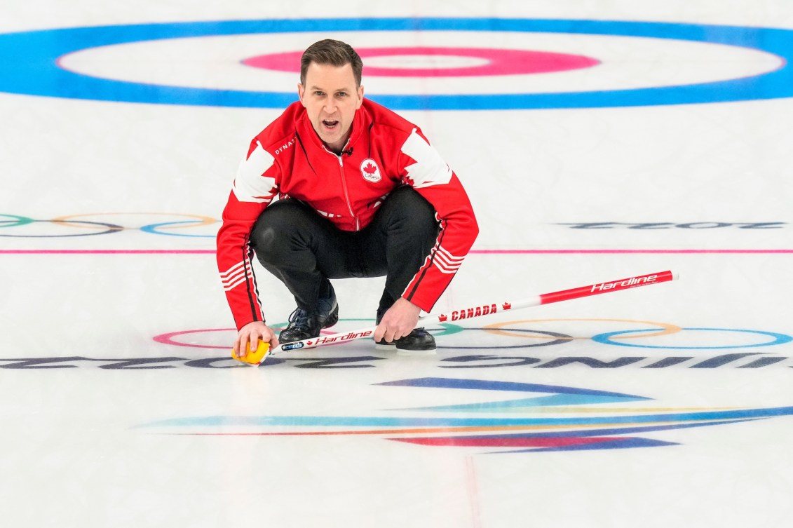 Le capitaine Brad Gushue d'Équipe Canada regarde sa pierre alors qu'il est accroupi et qu'il donne ses instructions aux brosseurs dans son match pour la médaille de bronze en curling masculin contre les États-Unis d'Amérique à Beijing 2022.