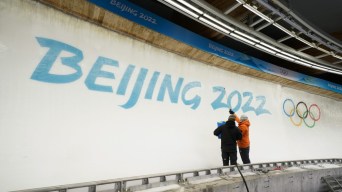 Deux hommes aspergent d'eau un mur de glace avec le logo de Beijing 2022.