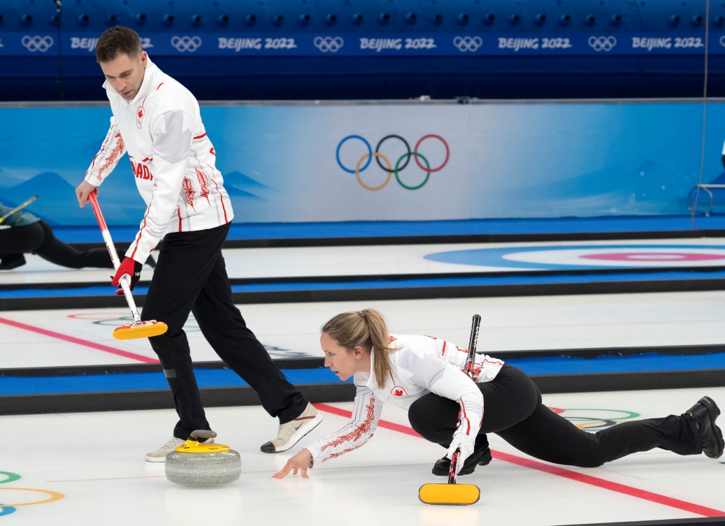 Une joueuse de curling lance la pierre à côté de con coéquipier qui tient son balai