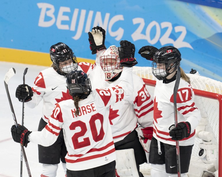 Trois joueuses canadiennes et la gardienne de but célèbrent leur victoire en tapant dans leurs gants.