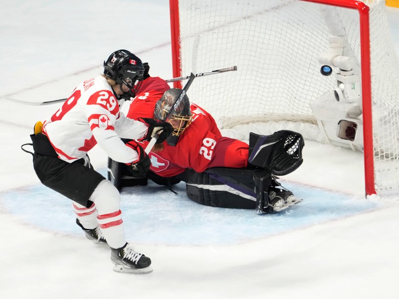 Seule devant le filet, l'attaquante du Canada Marie-Philip Poulin soulève la rondelle dans le haut du filet pendant que la gardienne suisse étend sa jambière et sa mitaine à Beijing 2022.