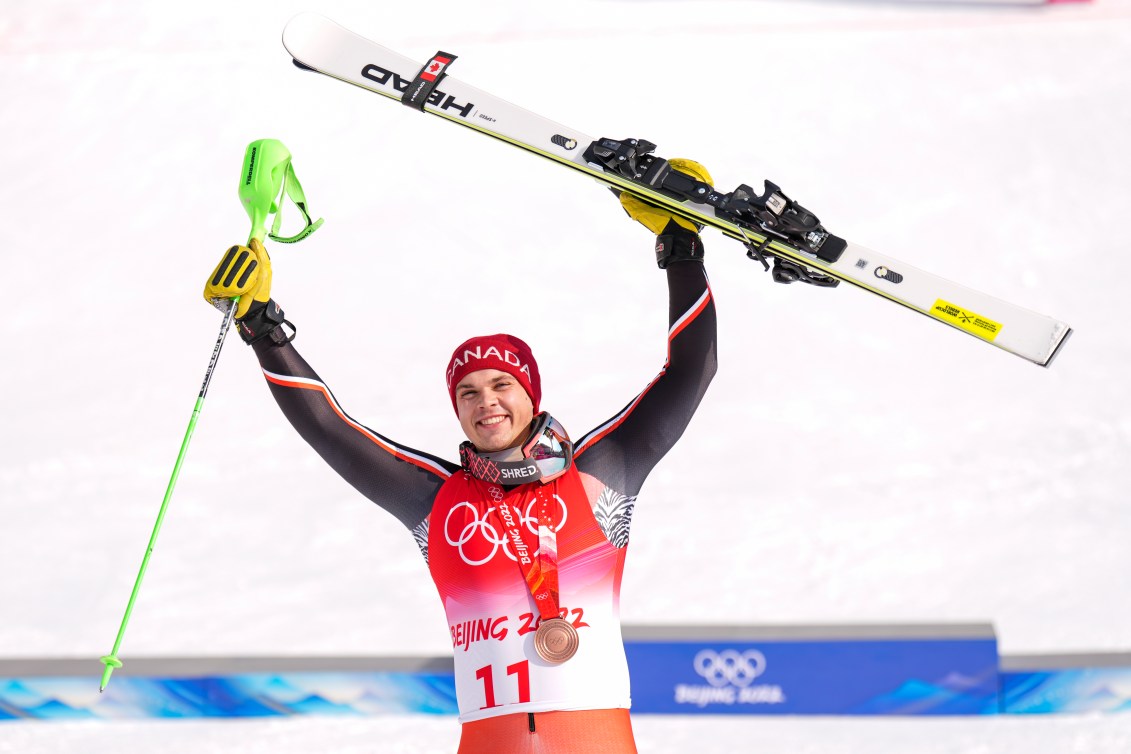 Le skieur alpin d'Équipe Canada Jack Crawford avec ses bâtons dans la main droite et ses skis (de descente)d ans la main gauche.