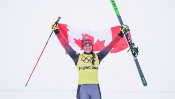 Marielle Thompson lève un bâton d'une main et un ski dans l'autre avec le drapeau du Canada haut dans les airs pour célébrer sa médaille d'argent gagnée au ski cross en ski acrobatique à Beijing 2022