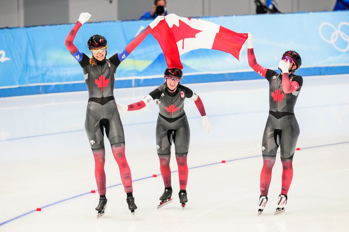 Trois patineuse sur la glace tiennent le drapeau canadien. 