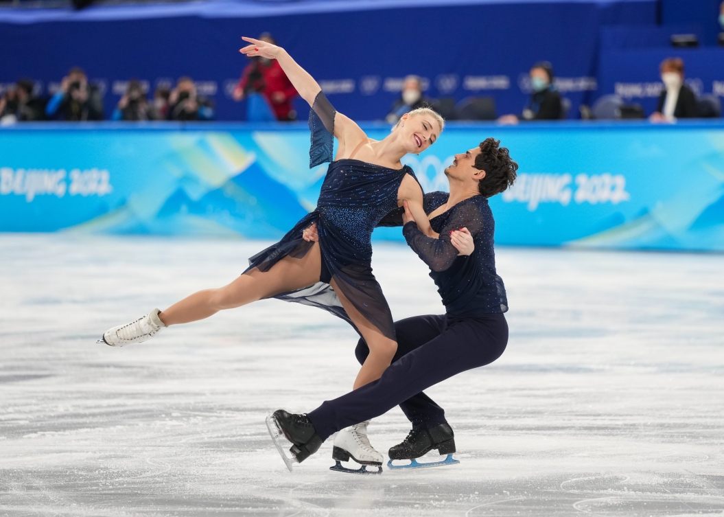 En patinage artistique, Piper Gilles fait une arabesque pendant que Paul Poirier lui tient le bras et la hanche en étant accroupi à Beijing 2022.