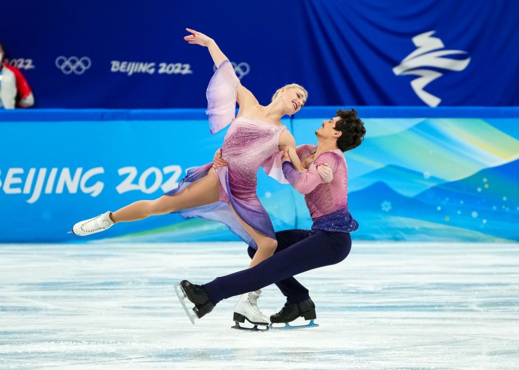 Piper Gilles d'Équipe Canada, fait une arabesque en levant le bras droit dans les airs et Paul Poirier tient Piper Gilles en étant accroupi et en patinant sur une jambe, à Beijing 2022.
