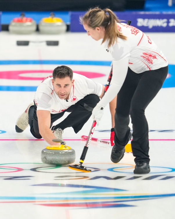 John Morris lance une pierre de curling pendant que Rachel Homan balaie au tournoi de curling double mixte des Jeux olympiques de Beijing 2022.