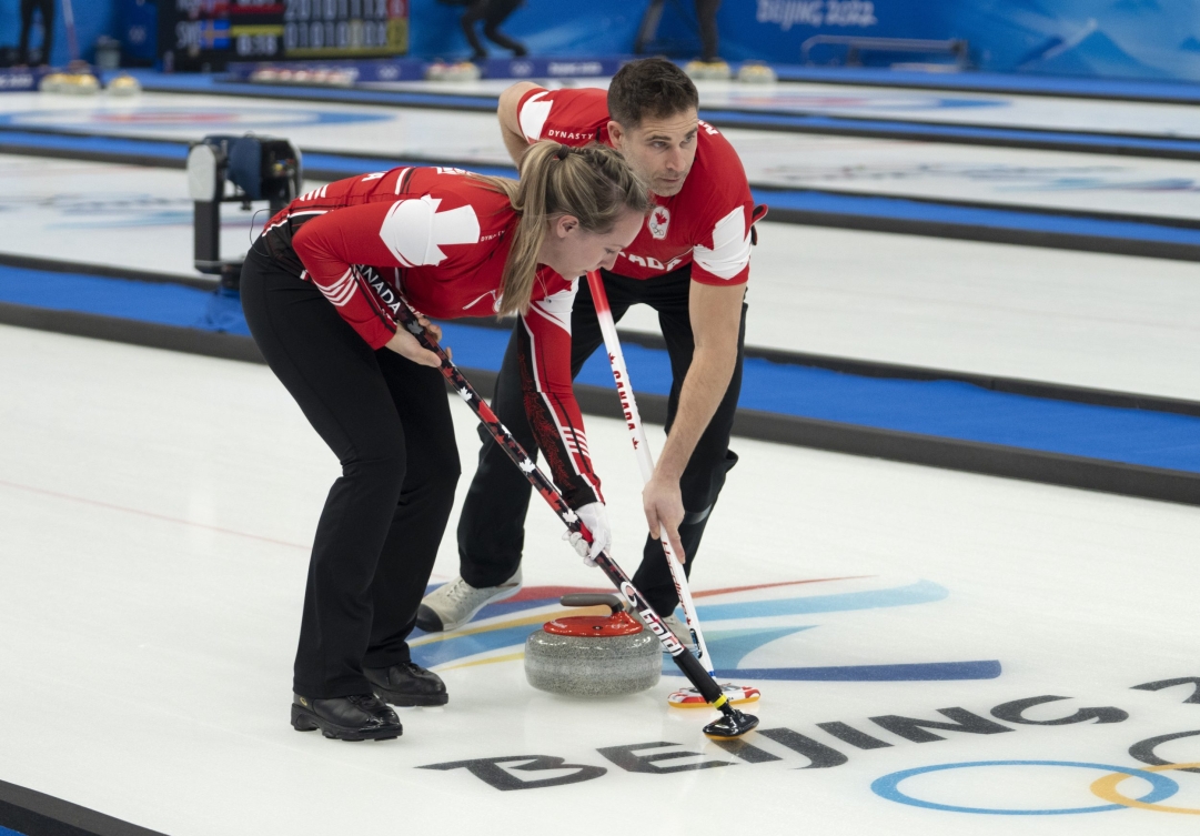 Les Canadiens Rachel Homan et John Morris balaient une pierre rouge en curling double mixte.