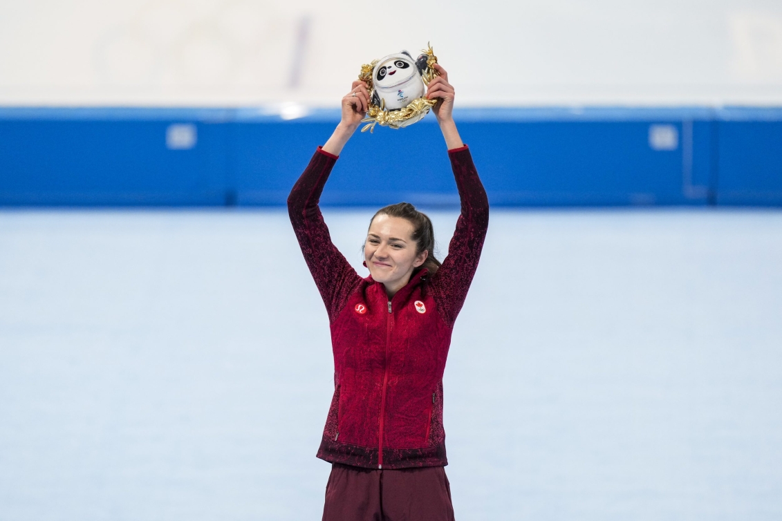 Isabelle Weidemann lève la mascotte de Beijing 2022 haut dans les airs avec le sourire pour célébrer sa médaille d'argent au 5000 mètres du patinage de vitesse sur longue piste.