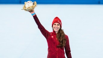 Ivanie Blondin célèbre sa médaille d'argent à l'épreuve de départ groupé en patinage de vitesse sur longue piste en levant la mascotte de Beijing 2022 haut dans les airs et avec le sourire aux lèvres sur le podium.