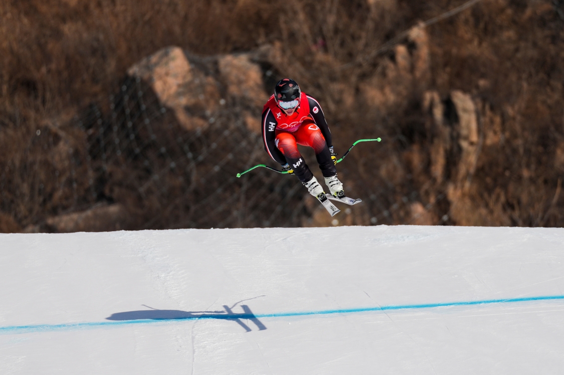 Le skieur alpin d'Équipe Canada Jack Crawford est dans les airs après un saut avec les mains derrière les genoux lors d'une descente à Beijing 2022.