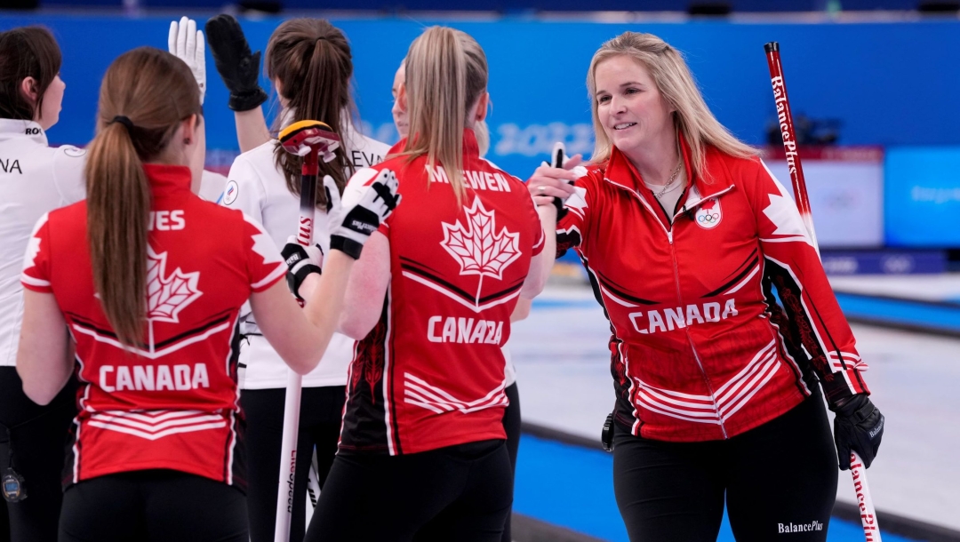 La capitaine canadienne Jennifer Jones lève la main pour serrer la main de sa coéquipière Dawn McEwen pour célébrer la victoire contre le ROC à Beijing 2022.