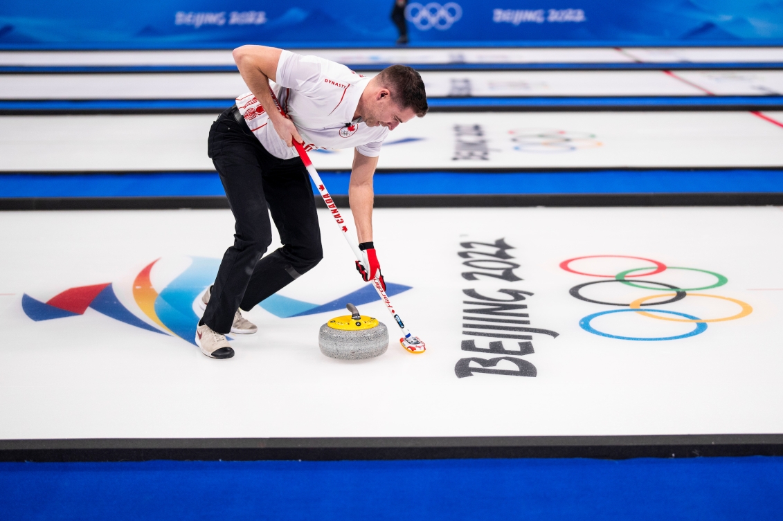 John Morris lance une pierre et balaie la glace au curling double miste.