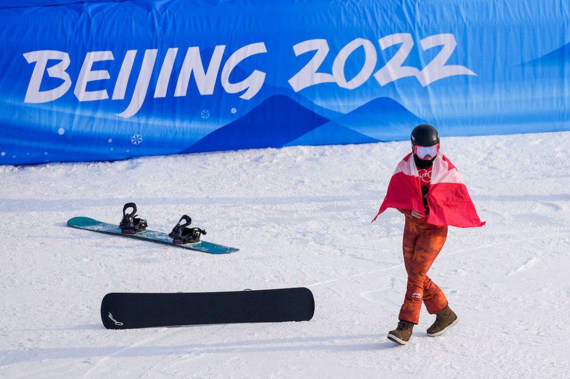 Drapé du drapeau canadien, Meryeta O'Dine marche devant une planche à neige laissée au sol après avoir atteint la troisième place du podium en snowboard cross féminin à Beijing 2022.