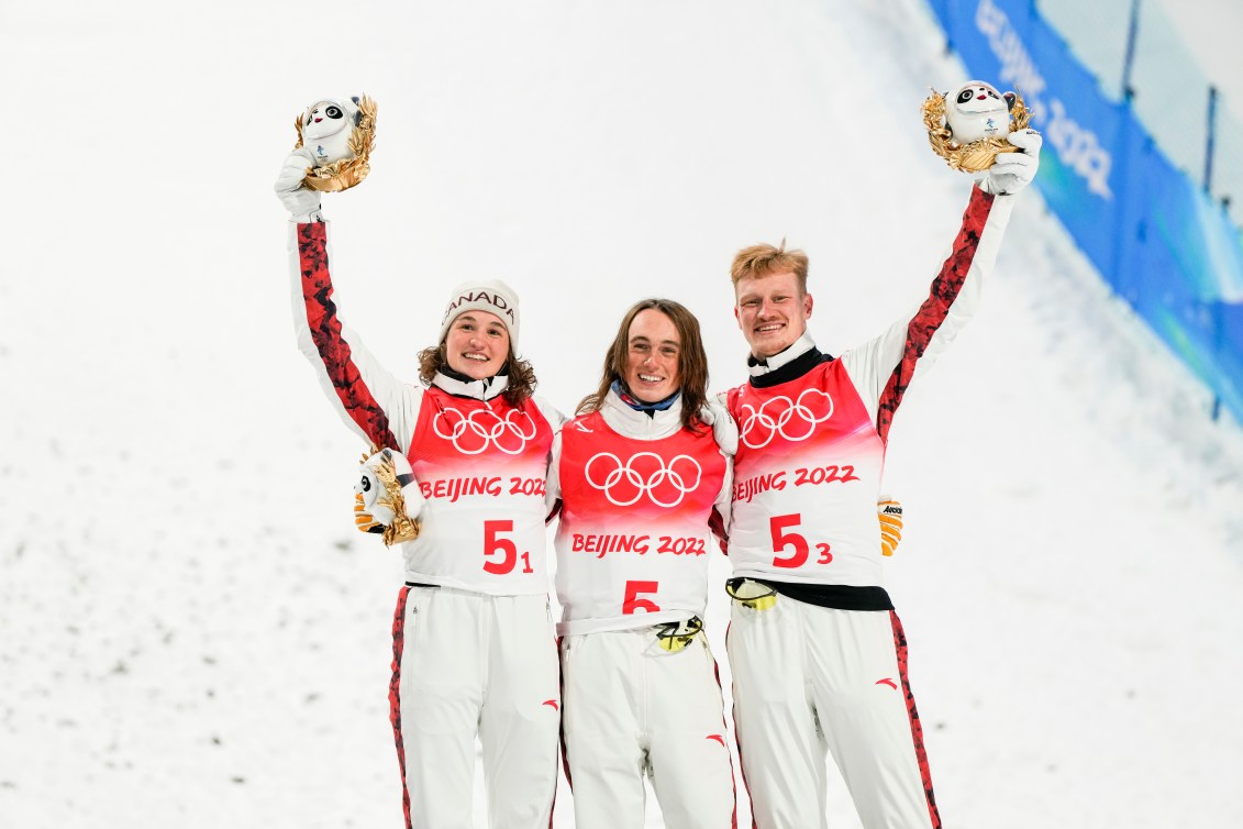 Marion Thénault, Miha Fontaine et Lewis Irving s'enlacent par les épaules sur le podium pour célébrer leur médaille de bronze au saut à ski par équipe mixte de Beijing 2022