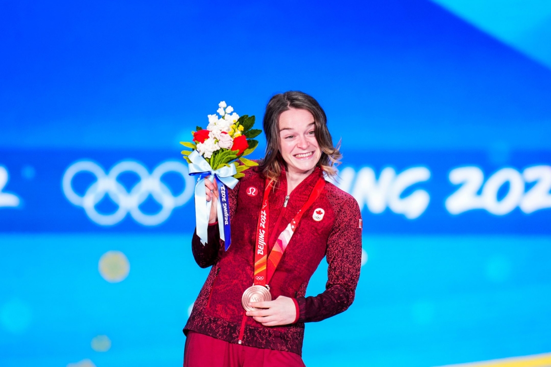 La patineuse de vitesse canadienne Kim Boutin sur le podium du 500 m courte piste. Elle soulève sa médaille de bronze avec la main gauche et tient son bouqut de fleurs avec la main droite.