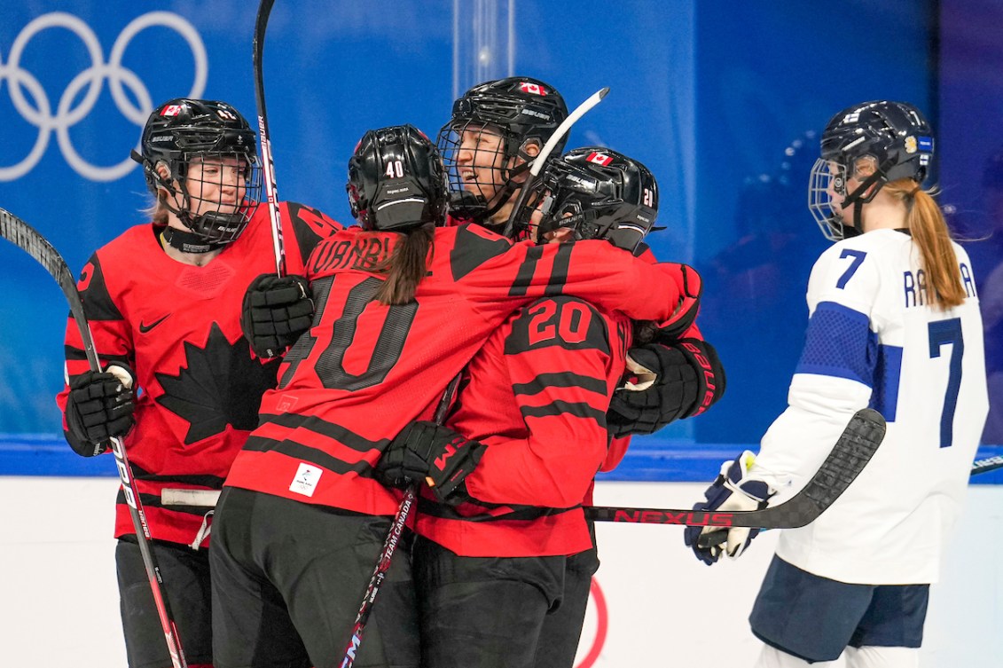 Quatre joueuses de hockey d'Équipe Canada célèbrent le but entre coéquipières et une joueuse de la Finlande patinent vers le banc. coéquipières