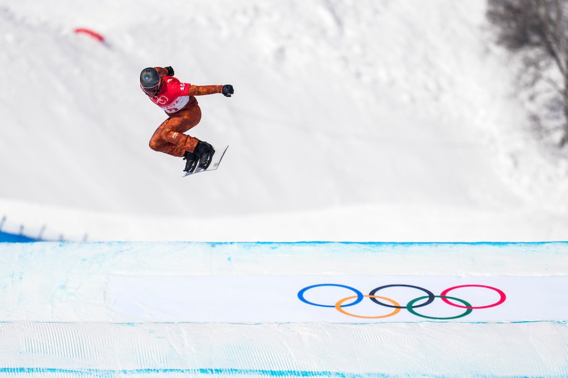 Le planchiste d'Équipe Canada Eliot Grondin saute dans les airs lors d'une course de snowboard cross masculin à Beijing 2022.
