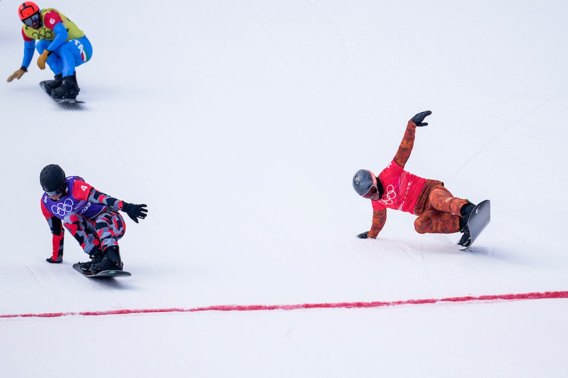 Le planchiste d'Équipe Canada Eliot Grondin lance sa planche en avant à la d'arrivée de la course de snowboard cross masculin à côté du médaillé d'or de la course à Beijing 2022.