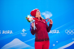 Christine de Bruin d'Équipe Canada sourit en regardant vers le haut et vers sa gauche sur le podium du monobob féminin, en tenant son bouquet de fleurs et sa médaille de bronze, à Beijing 2022.