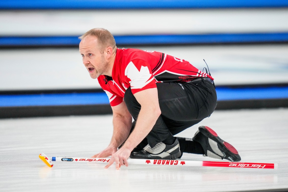 Mark Nichols, accroupi et les mains appuyées contre la glace, regarde son tir de loin et crie à ses coéquipiers lors du match de curling masculin contre les États-Unis à Beijing 2022.